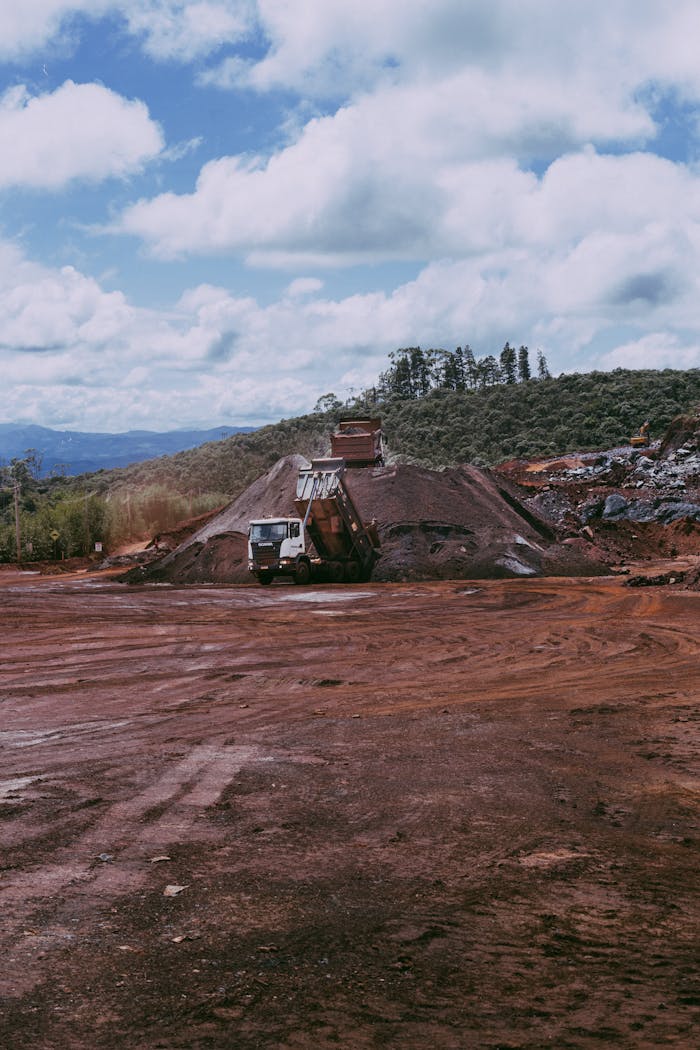 Mastering the First Impression: Your intriguing post title goes here Wide view of a mining site with dump trucks and red dirt, under a cloudy sky.